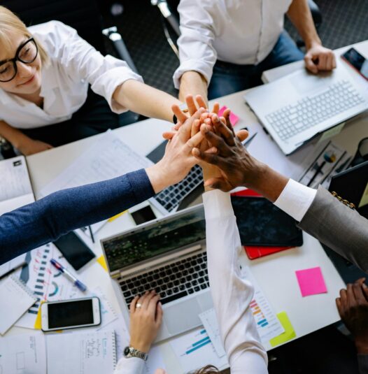 A group of diverse professionals high-fiving over a collaborative workspace.